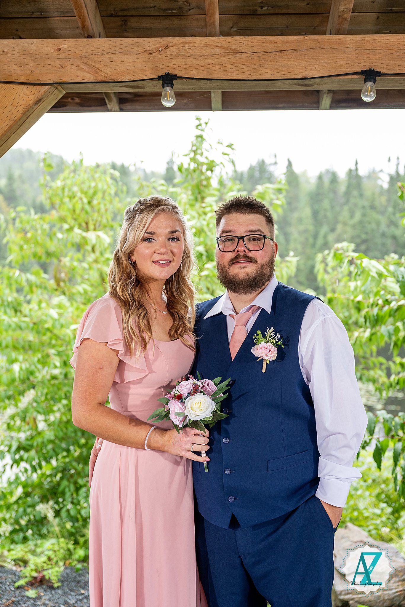 A bridal party member in pink poses with a groomsman in navy blue vest at an outdoor wedding venue.