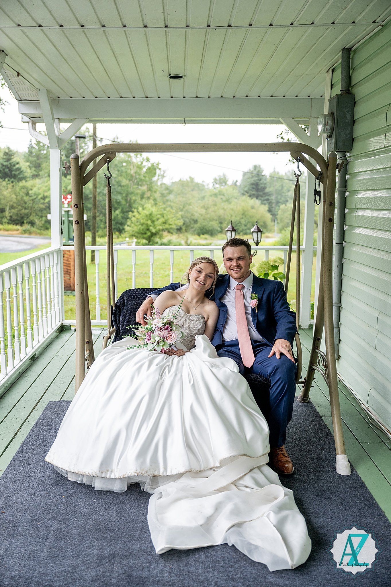 Wedding couple poses playfully along white covered porch with elegant white gown and navy suit.