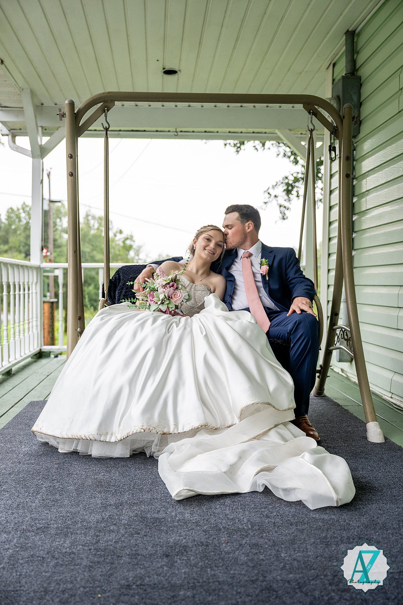 Wedding couple lies together posing for artistic shots on porch with white dress flowing around them.