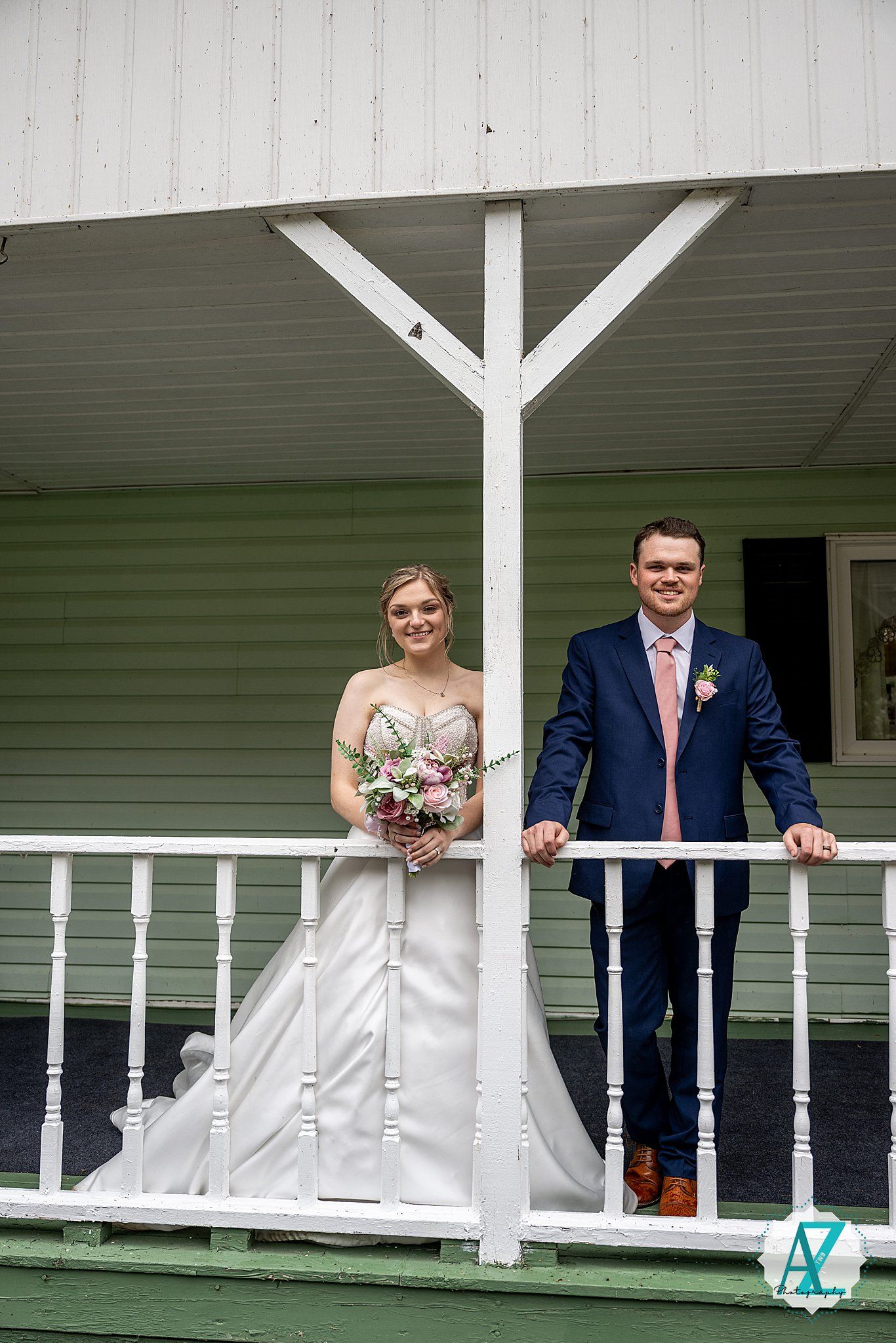 Wedding couple and party members pose along white railing of country porch.