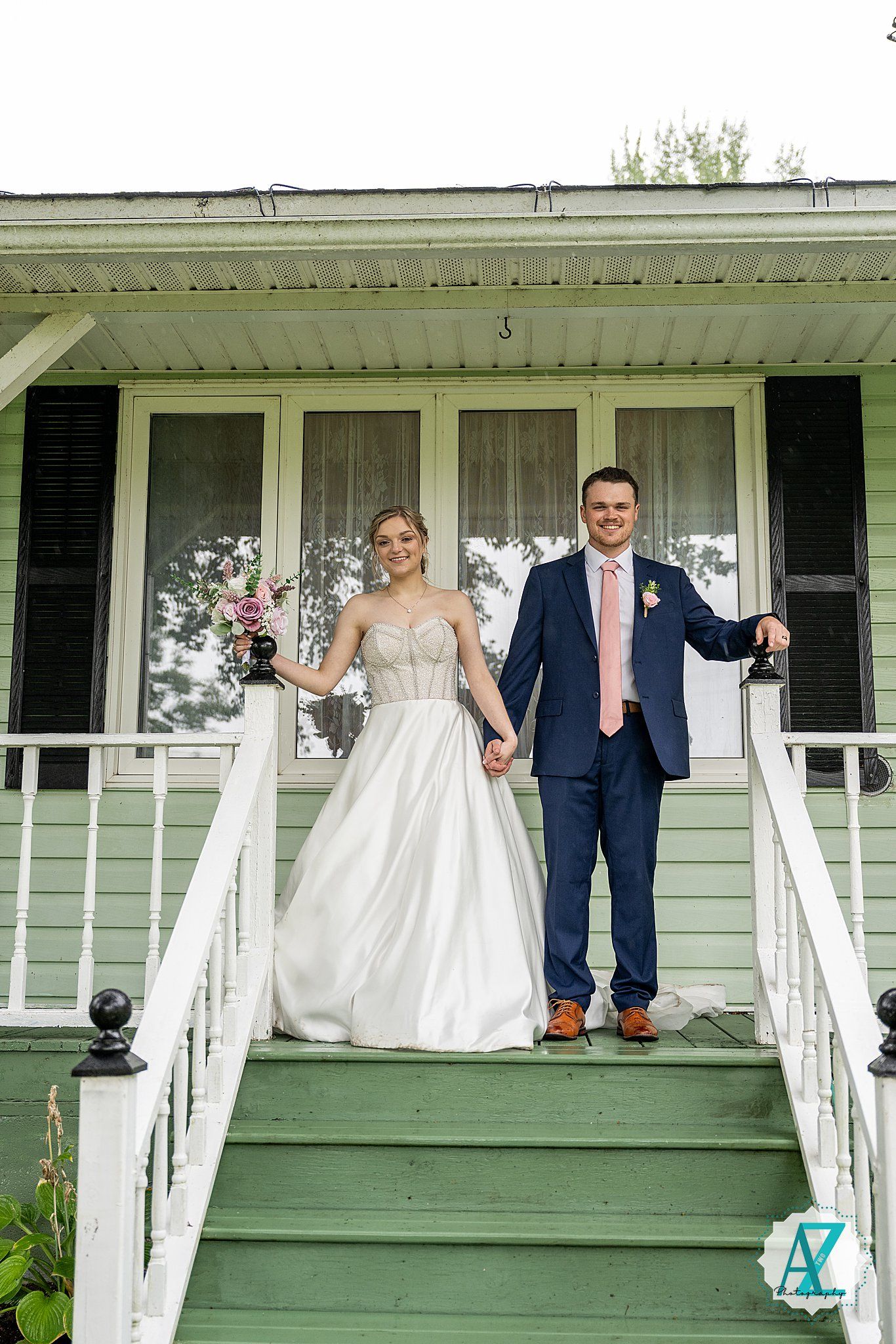 Couple strikes a series of joyful poses on a rustic farmhouse porch with white railings and mint green siding.