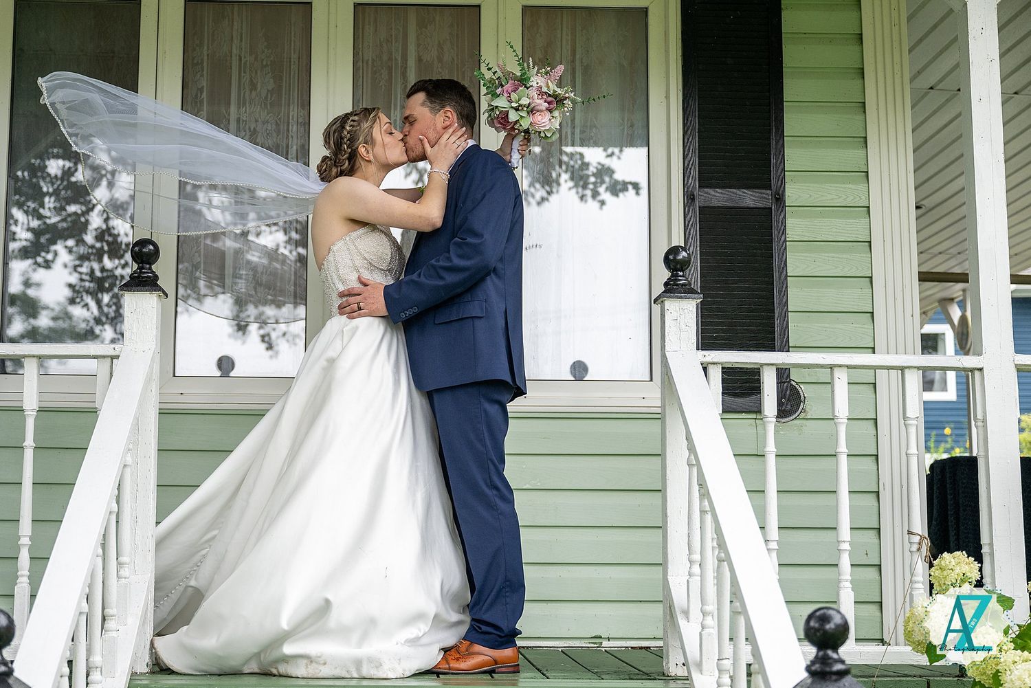 A romantic moment between a couple in wedding attire on a charming green front porch during their special day.