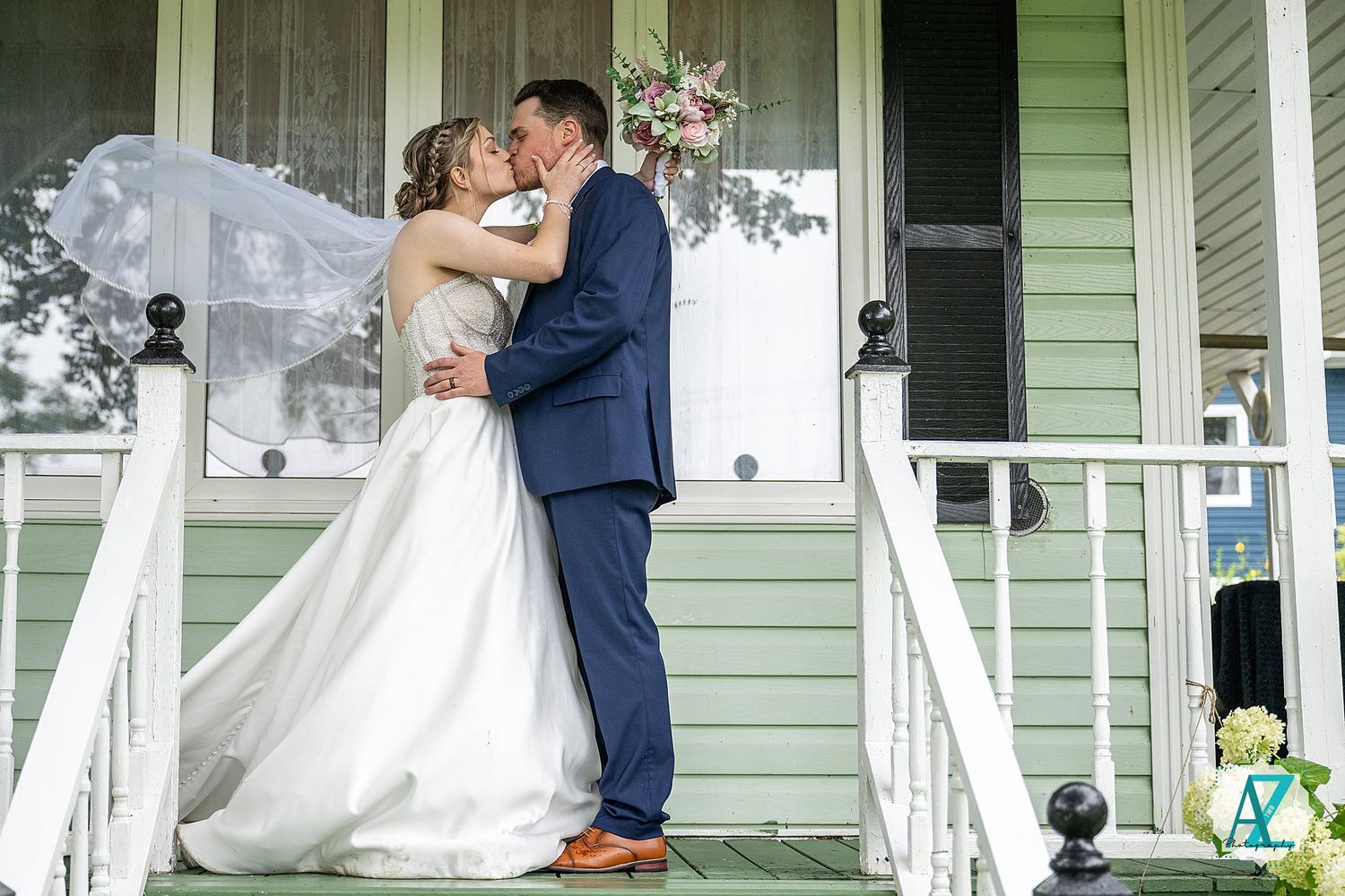 A romantic moment shared between a couple in wedding attire on a columned porch decorated with white fabric.