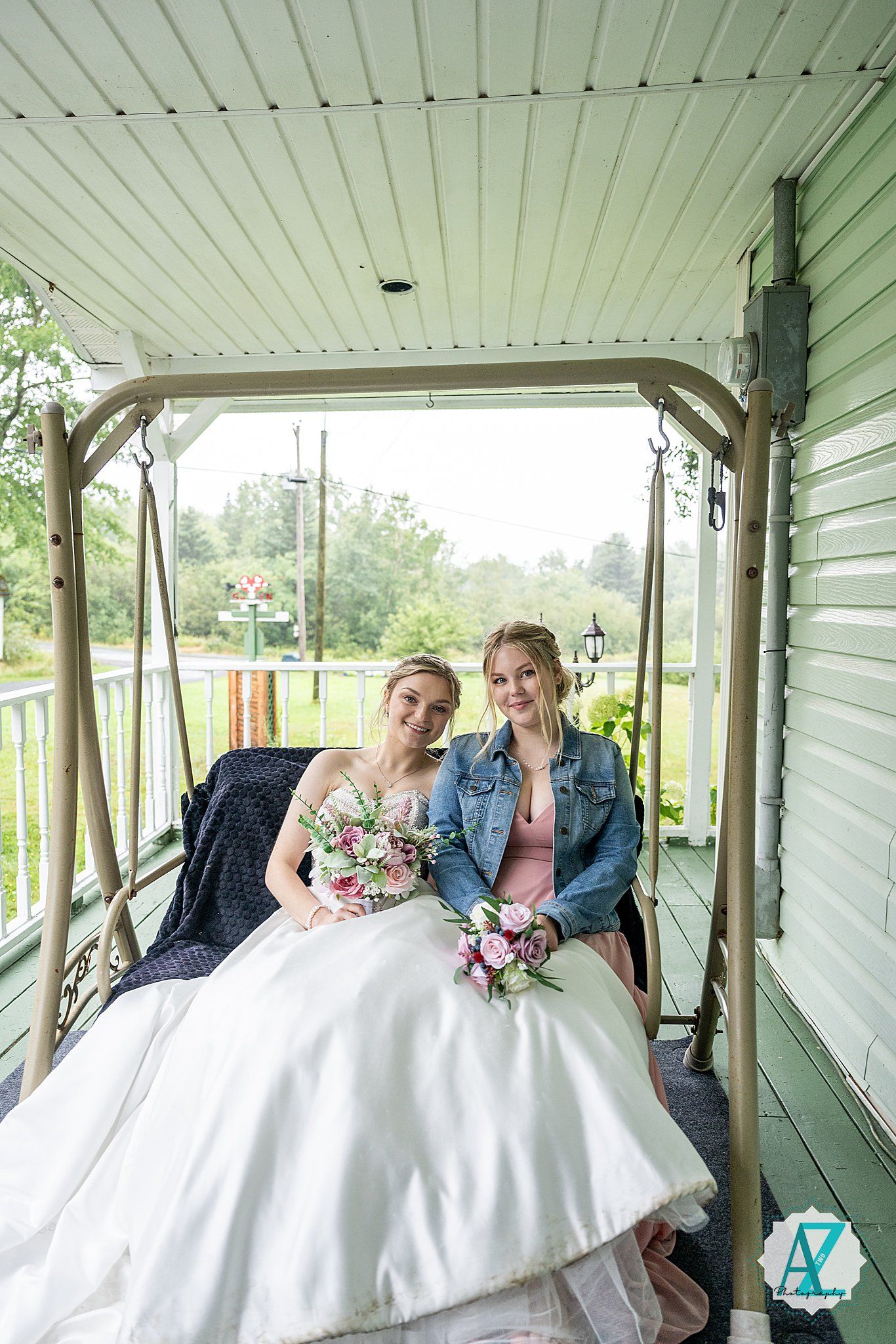 A couple sits together on a white porch swing decorated for a wedding with floral bouquets and denim accents.