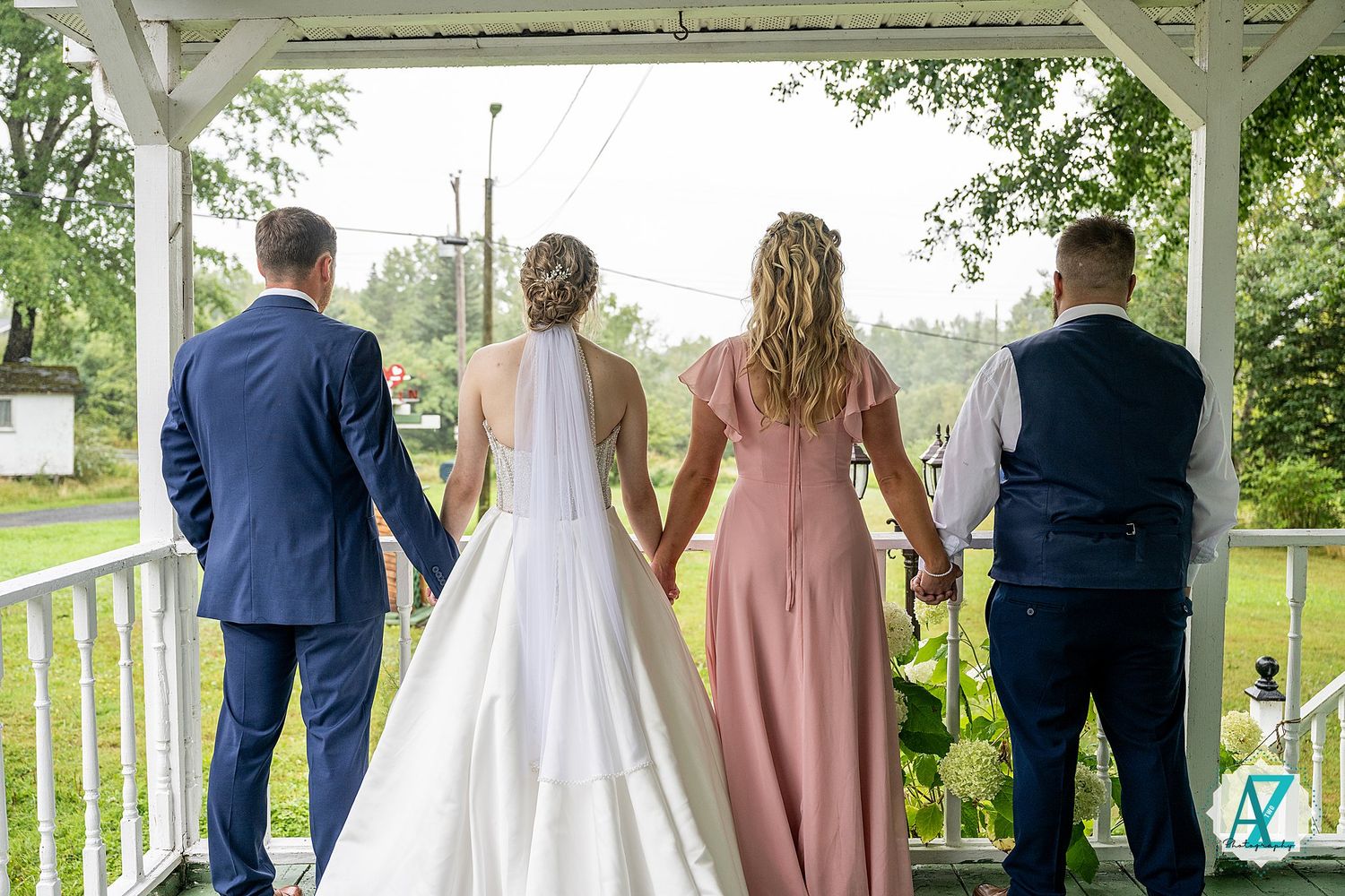 Wedding party gathered on a white gazebo porch overlooking scenic countryside views.