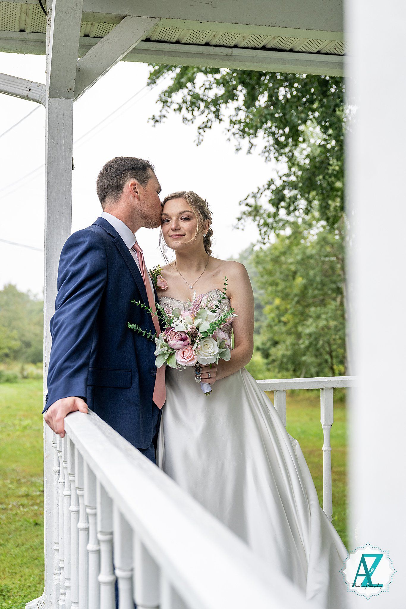 A romantic wedding couple shares a tender moment on a white porch surrounded by greenery on their special day.
