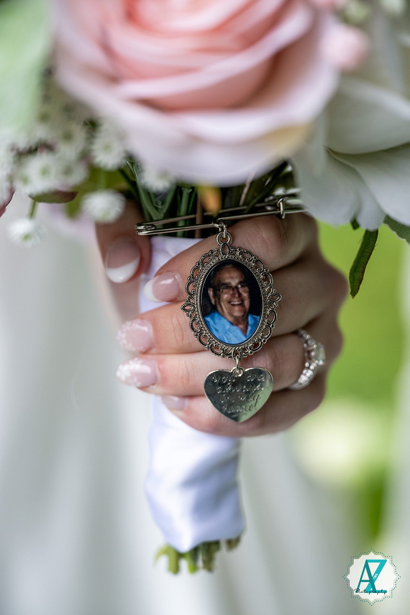 Close-up detail of pink roses and a vintage locket pendant at a wedding.