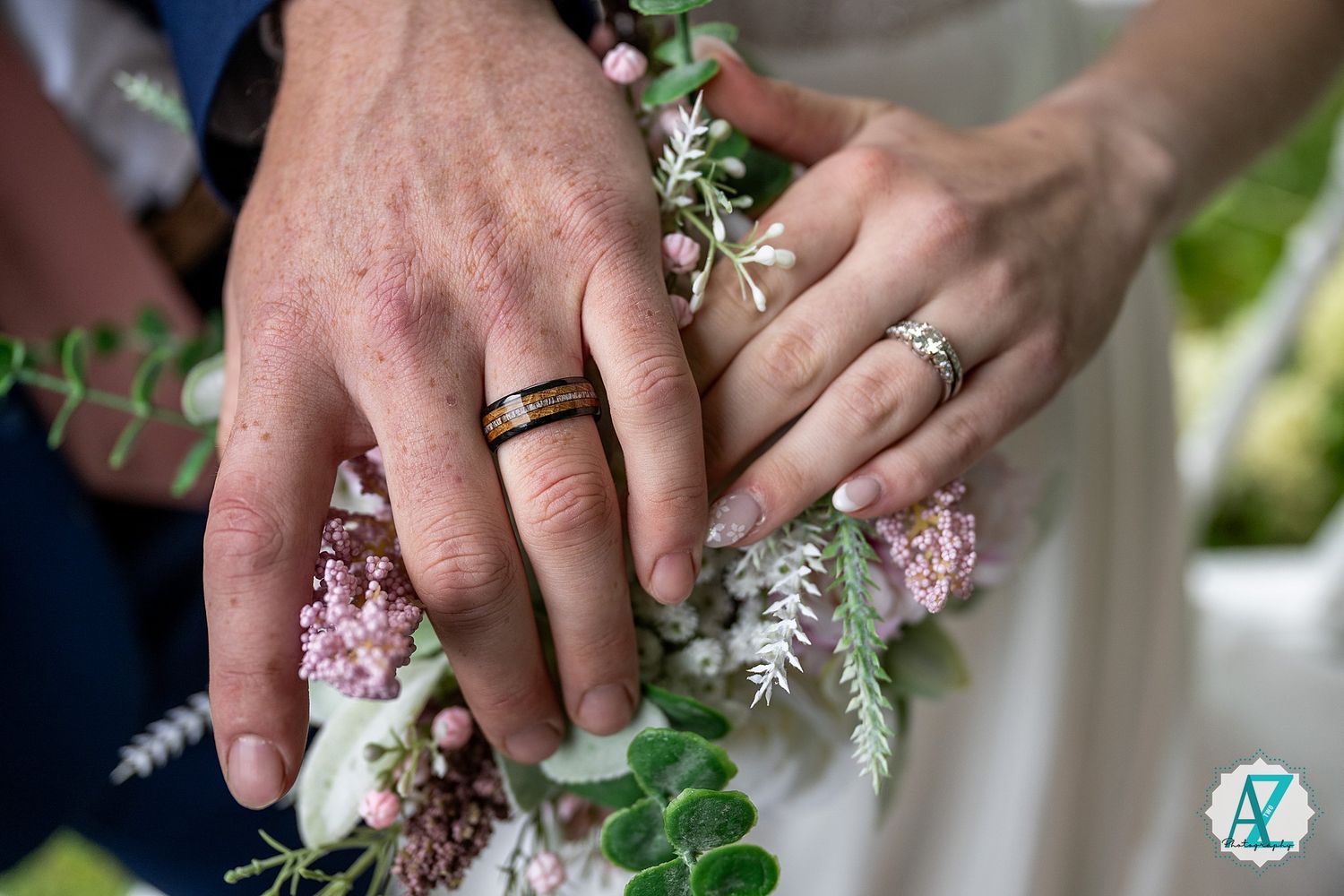 Close up of wedding rings and hands holding a delicate pink and white floral bouquet.