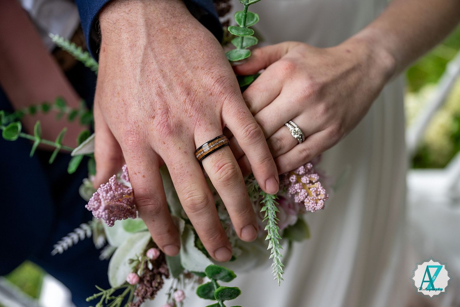 Close-up view of hands holding delicate pink and white floral wedding bouquets against greenery.