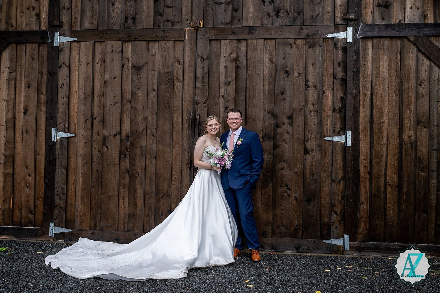 Wedding couple poses against rustic wooden barn wall backdrop for formal portraits.