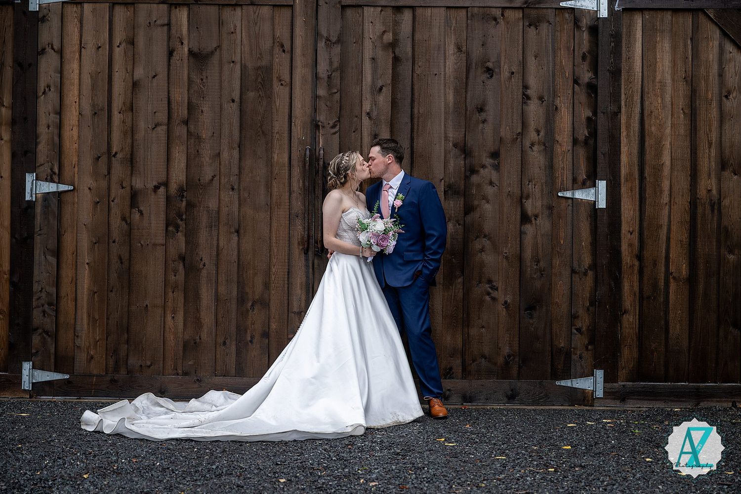 A couple shares an intimate moment at their wedding celebration against a rustic wooden fence backdrop.