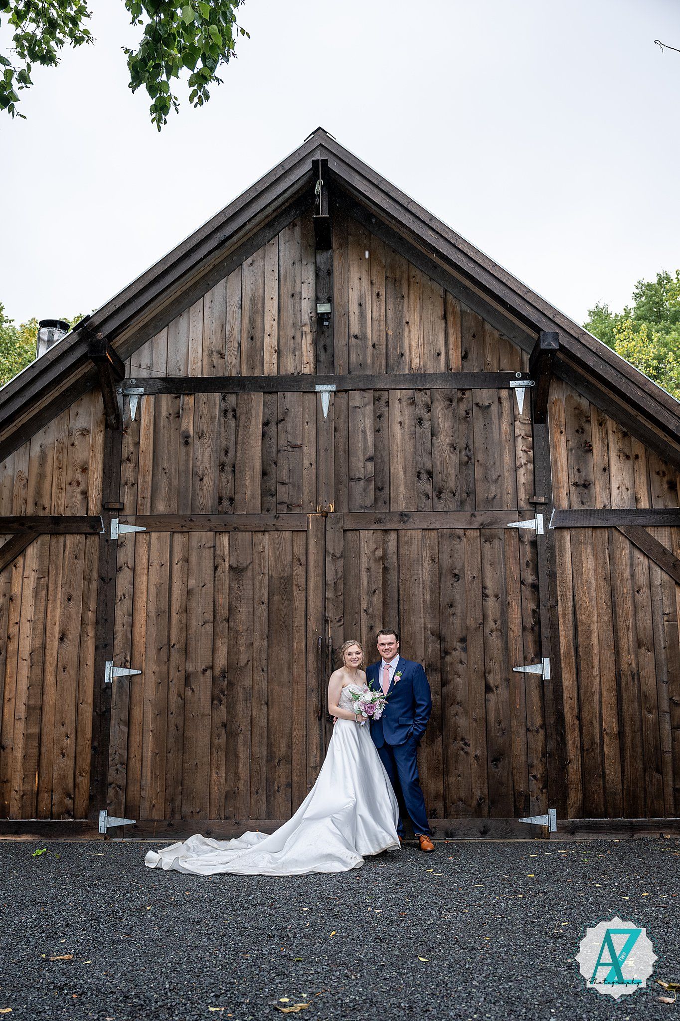 Classic wedding portrait series in front of dark wooden barn with gravel foreground.