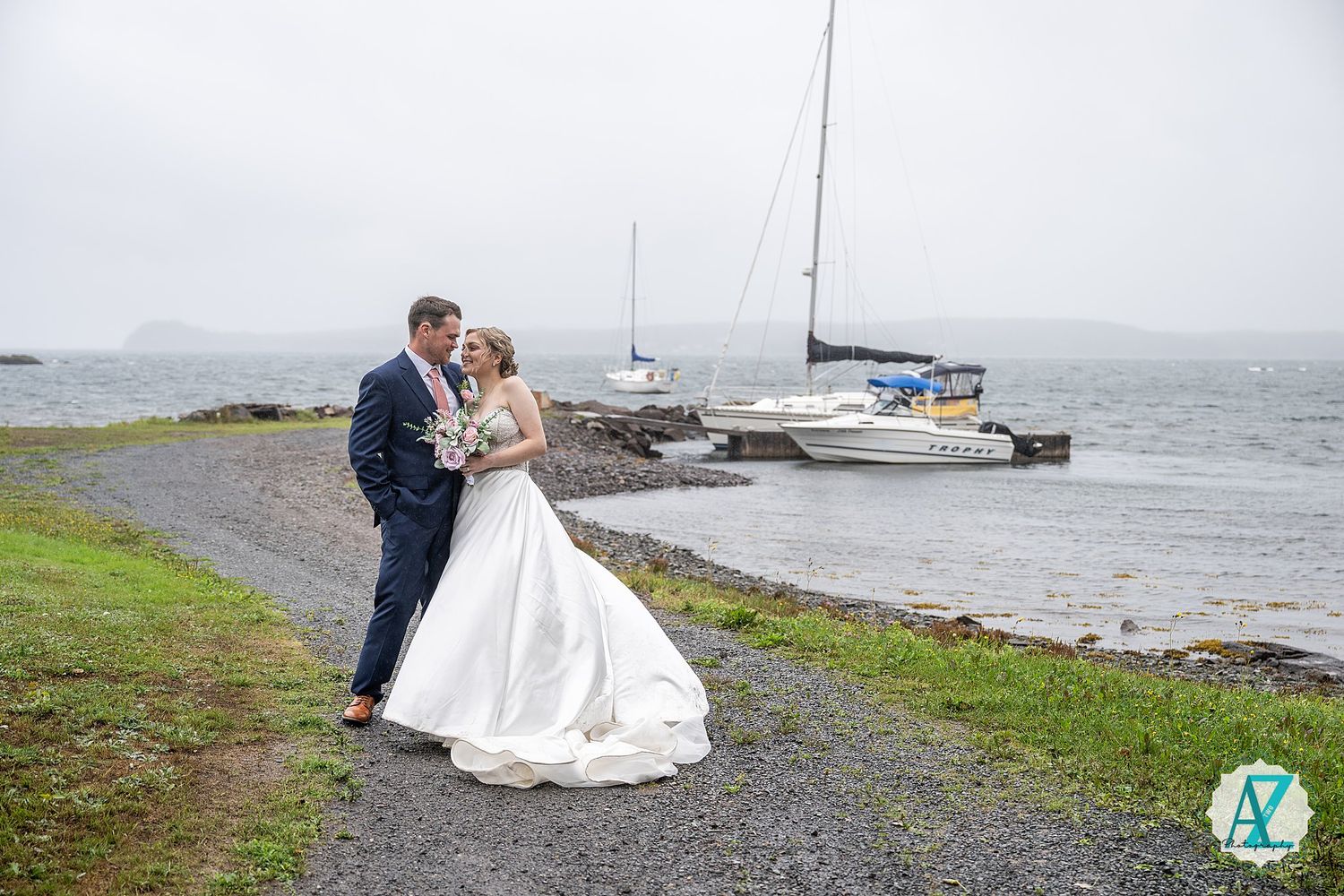 Romantic wedding photo session at a scenic coastal location with boats in the harbor and overcast skies.