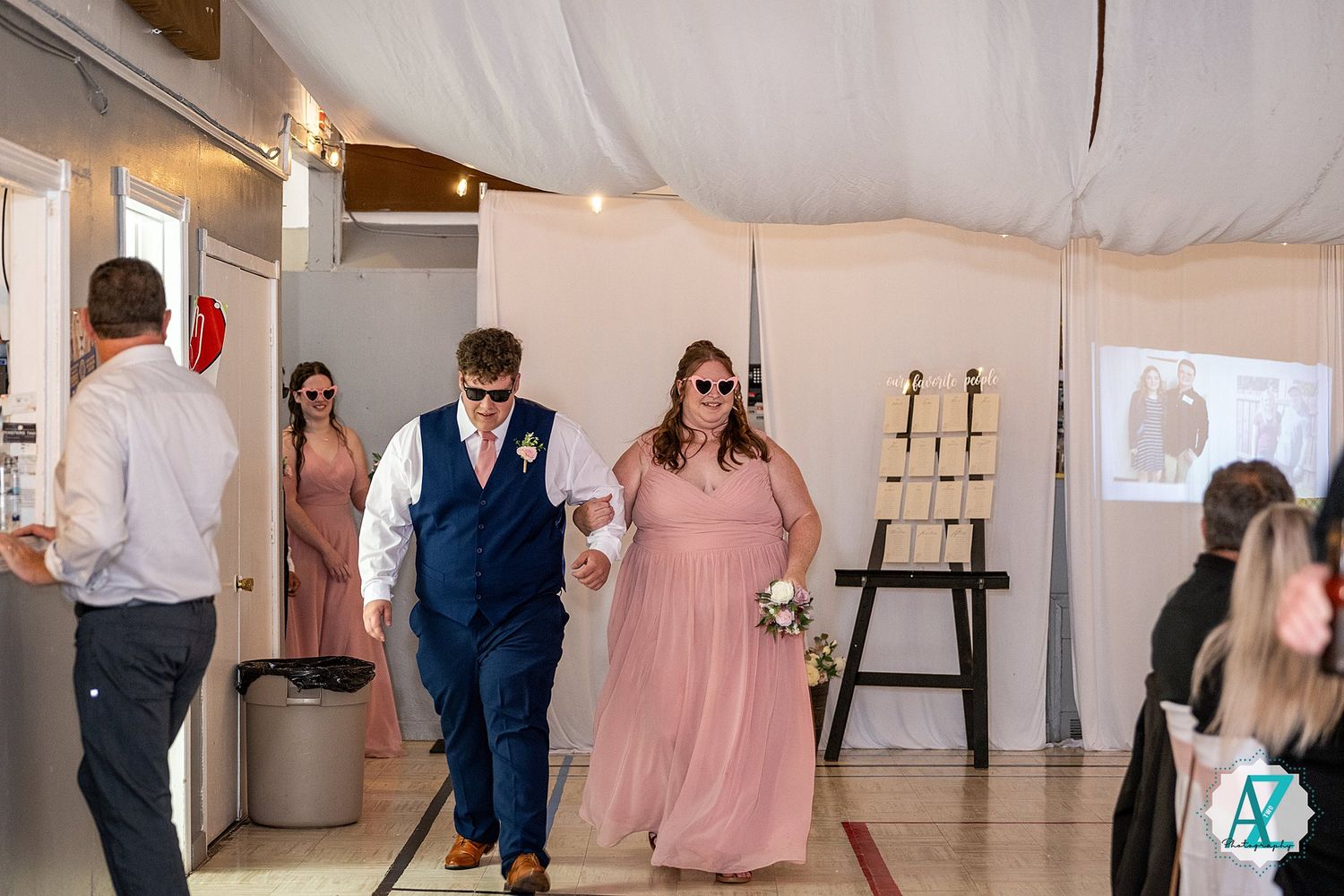 Wedding reception guests dance and celebrate under an elegant white tent at an outdoor venue.