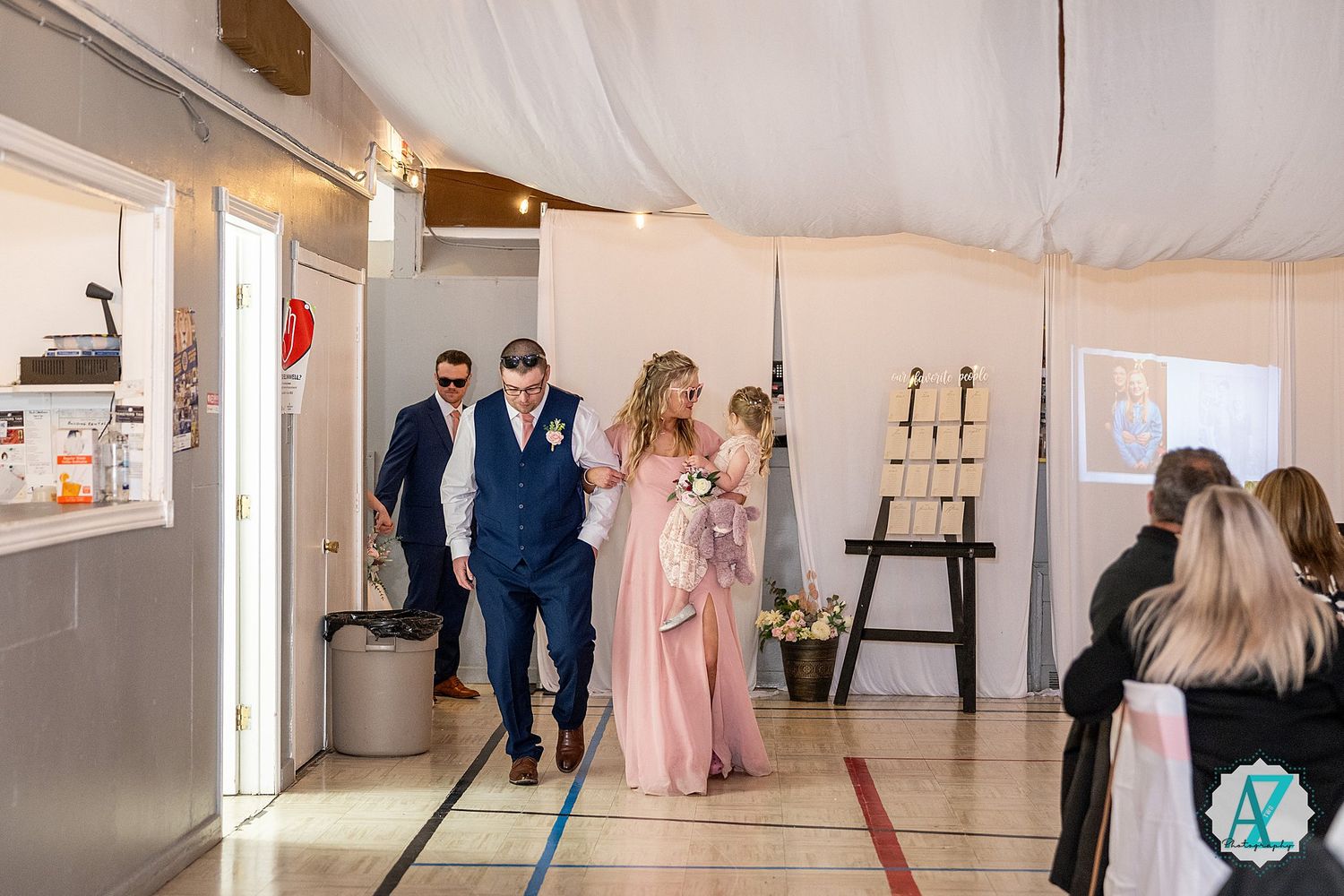 Large indoor reception space with string lights and white decor showing guests mingling during an event.