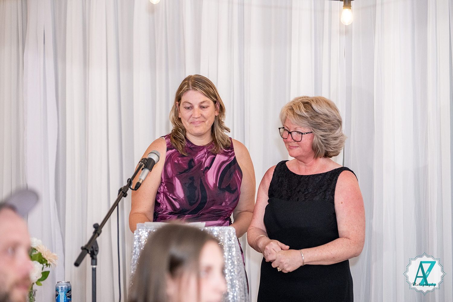 Group of wedding guests smiling and socializing at an elegant reception with white drapes in background.