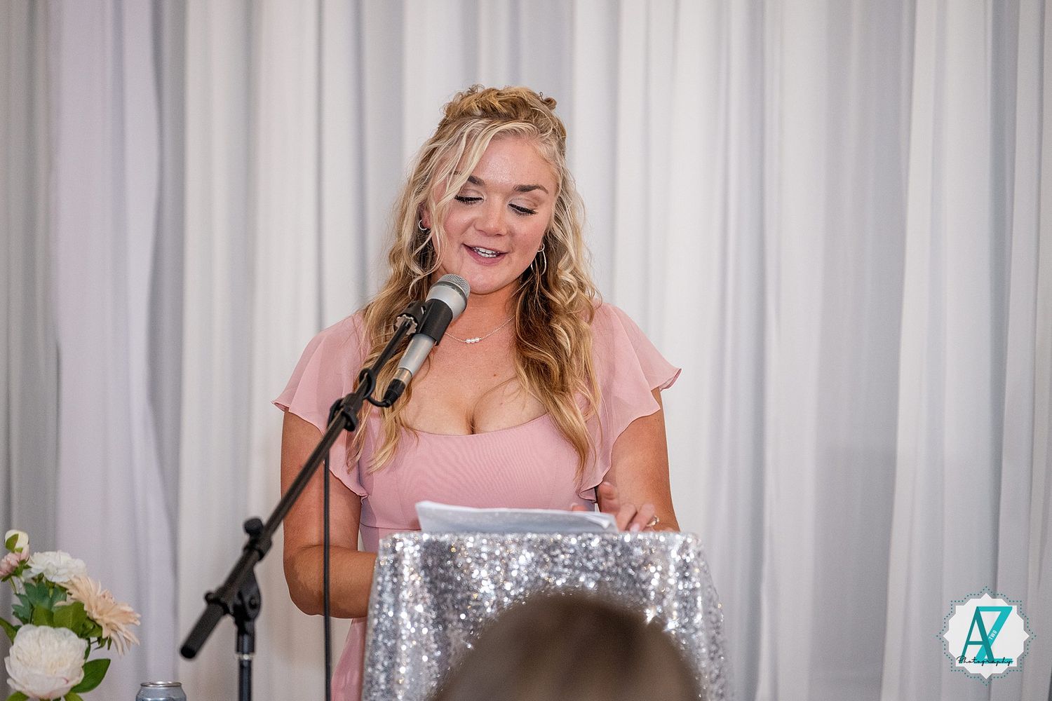 Wedding celebration scene with white backdrop and soft lighting during reception speeches.