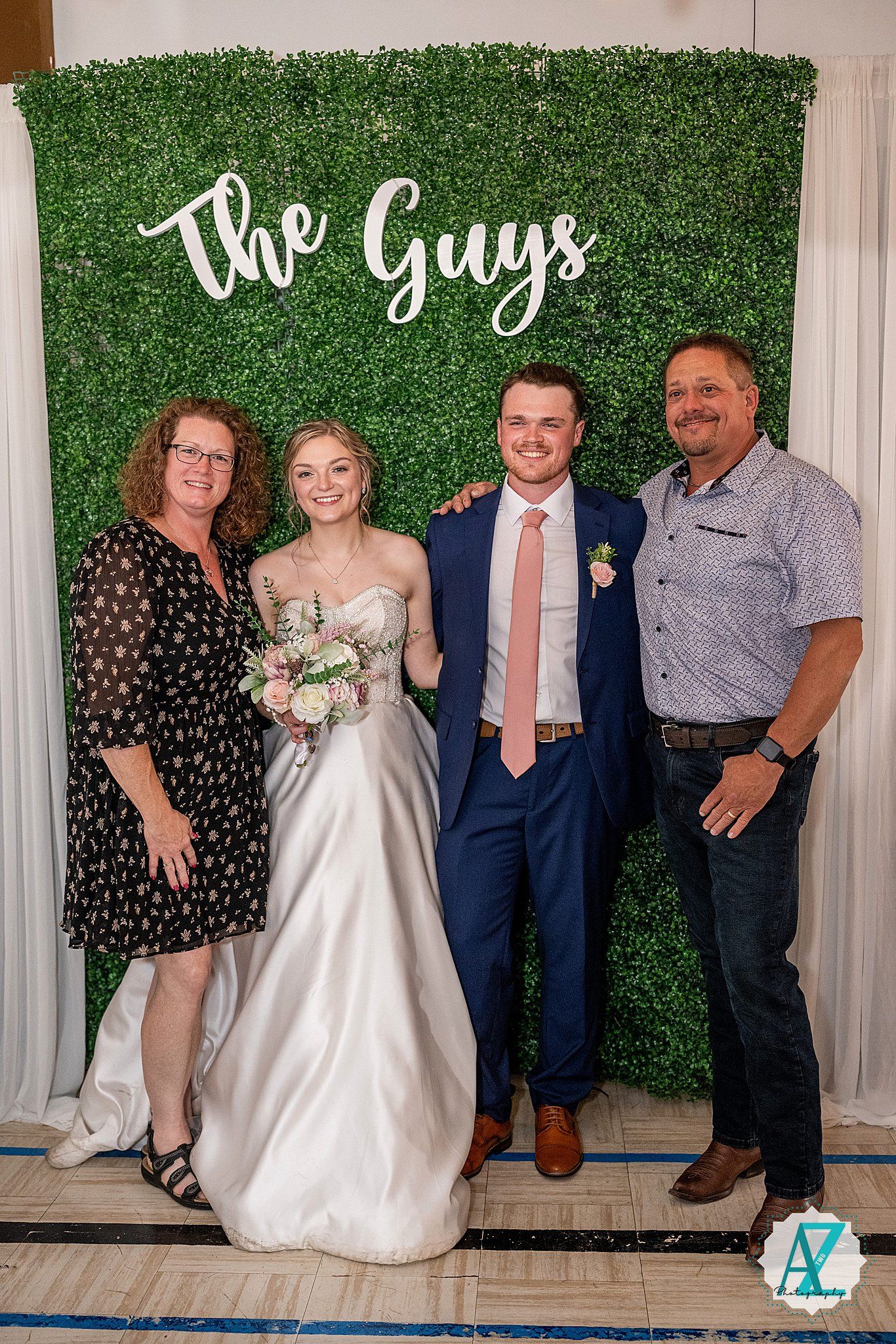 Wedding guests posing for group photos against a leafy green wall backdrop with white drapes.