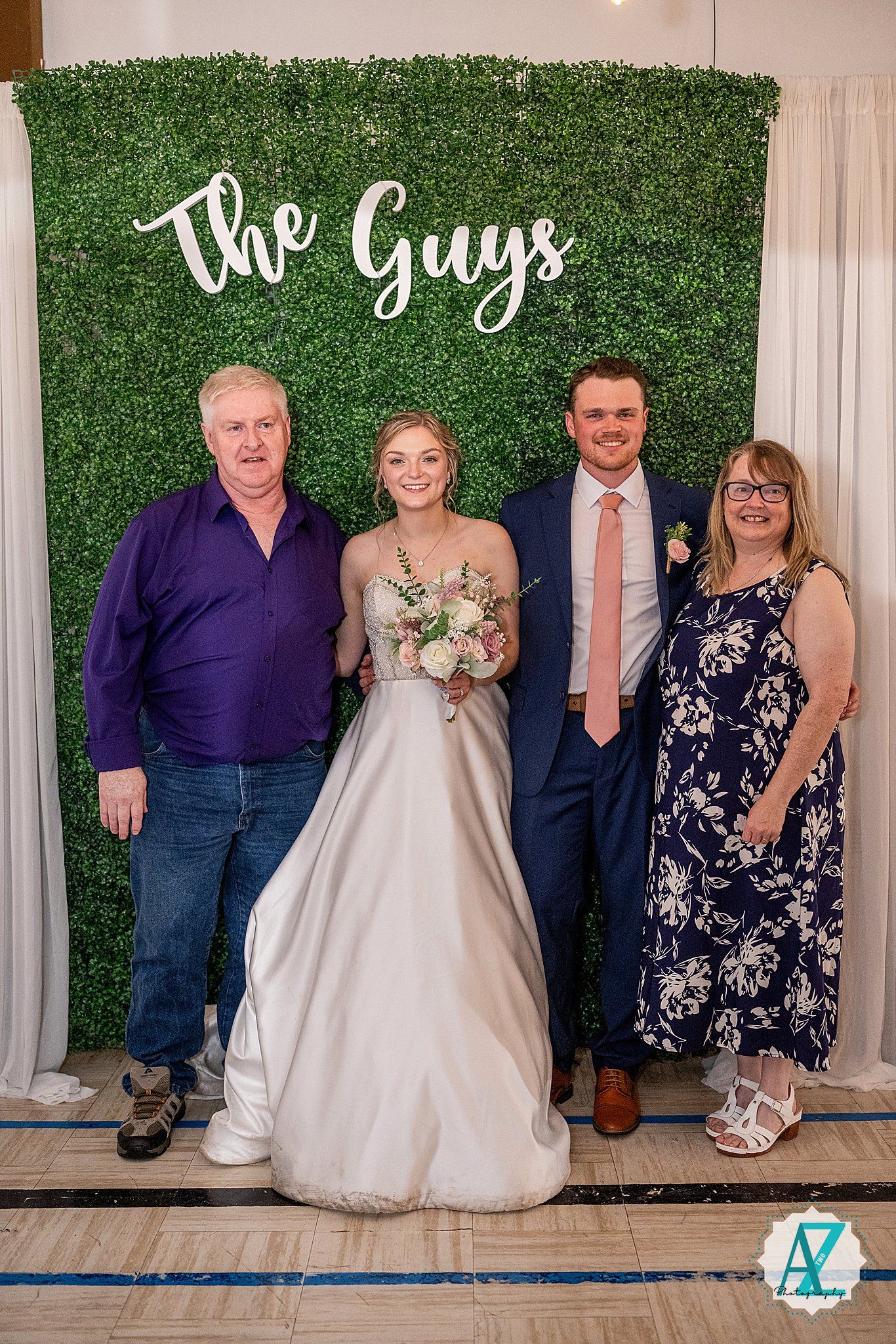 Wedding party members gather for formal photos in front of an artificial green wall with white curtains.