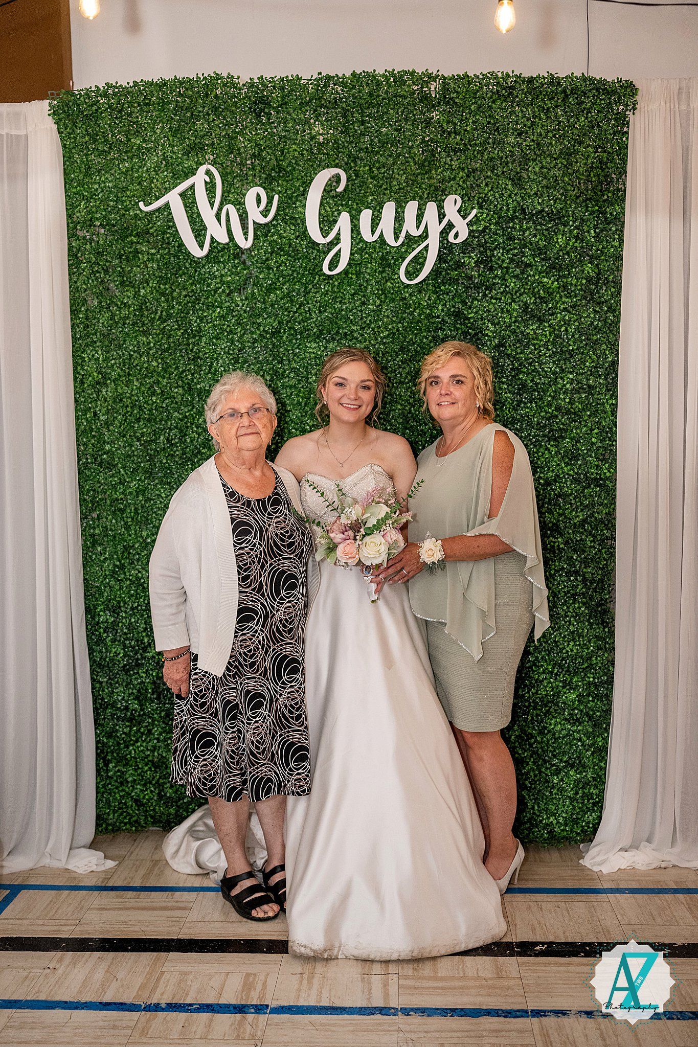 Wedding group photo featuring bridesmaids in blue dresses and bride in white gown against botanical wall decor.