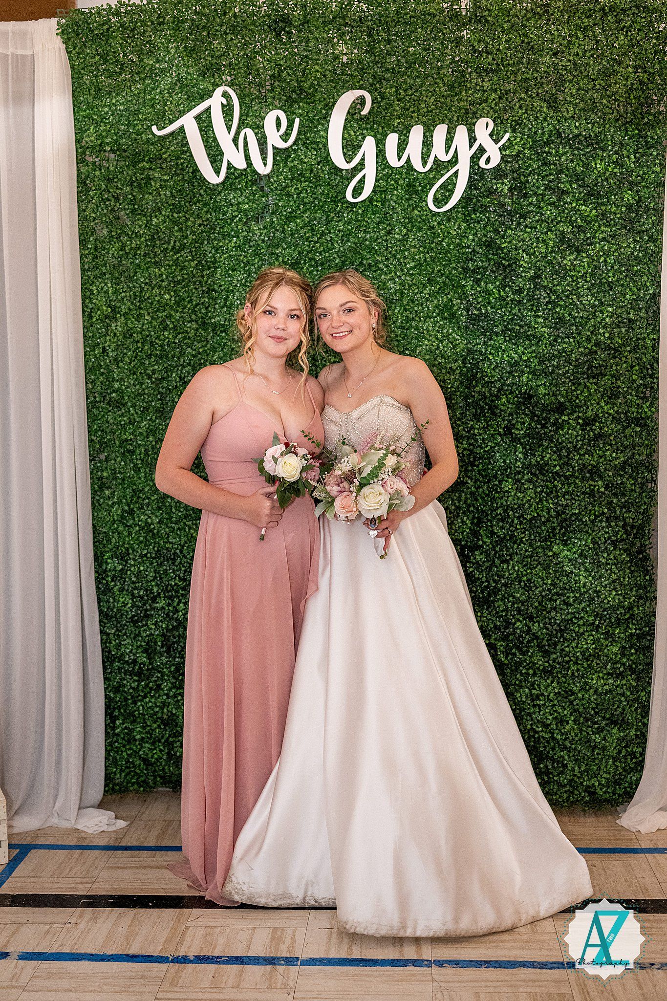 Wedding photo with two people in formal attire posing against a green hedge wall with "The Guys" text display.
