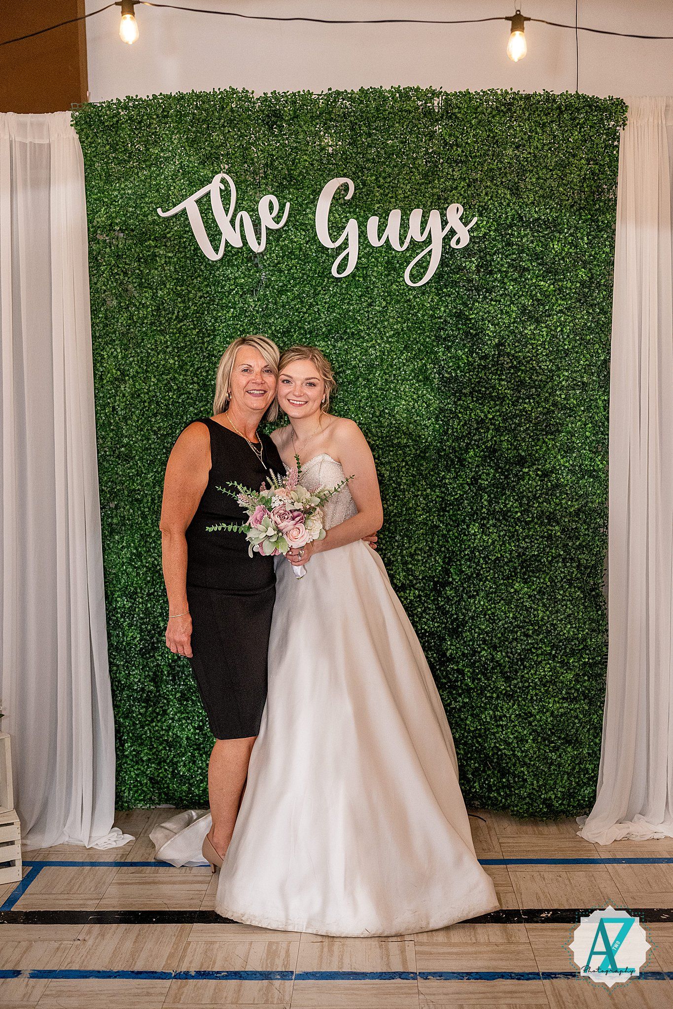 Wedding reception photo backdrop with artificial grass wall and 'The Guys' text for guest pictures.