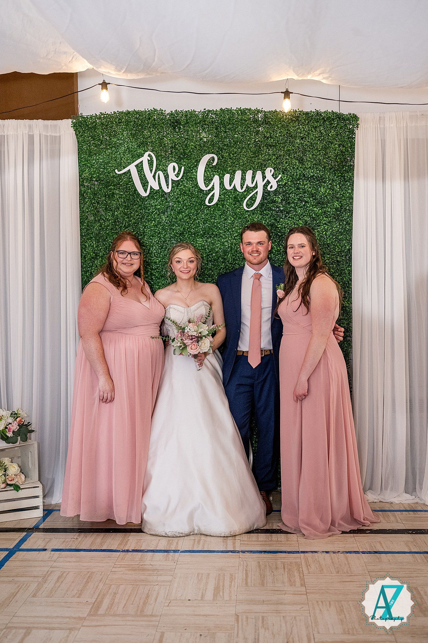Wedding party lineup against a white curtain backdrop with green hedge wall accent.