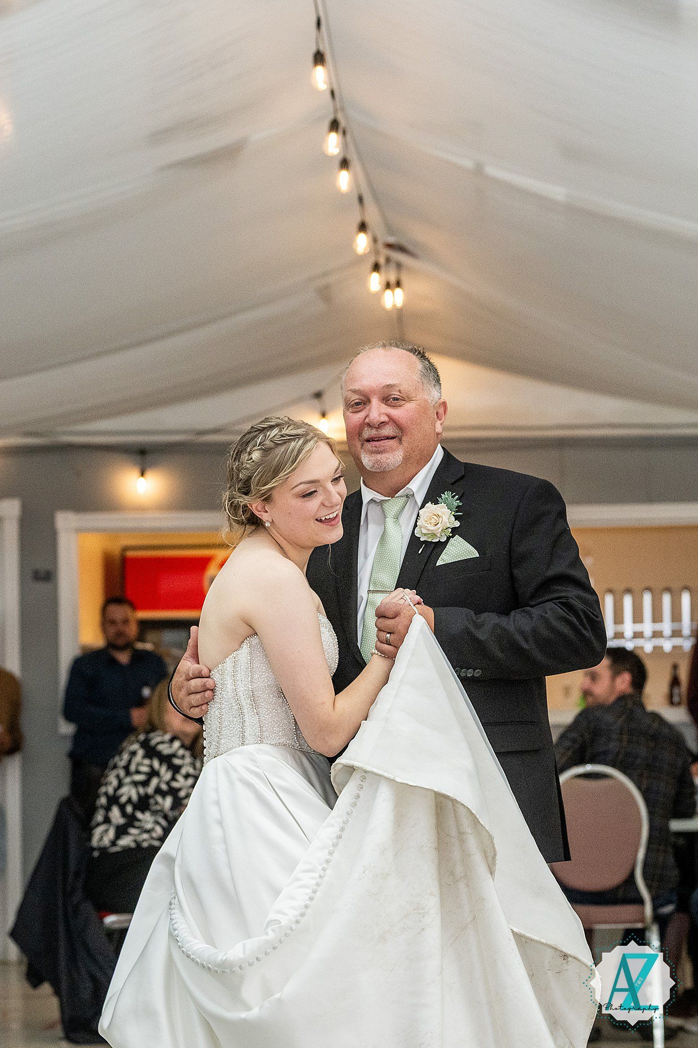A tender father-daughter dance at a wedding reception under strings of glowing lights.