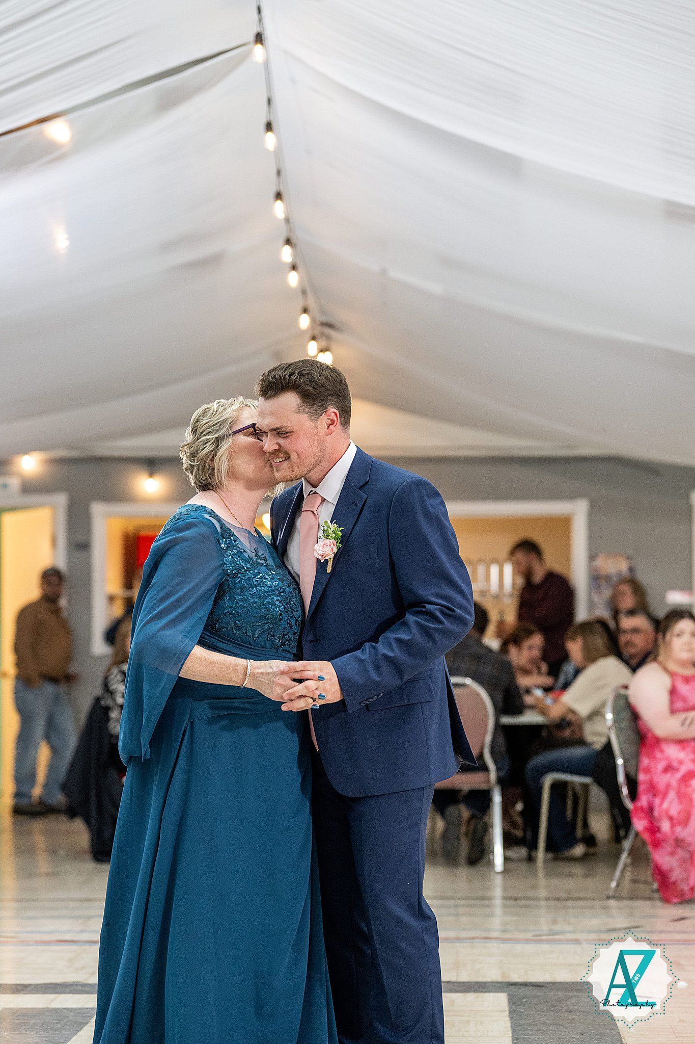 Guests dance together during a formal celebration in an elegantly decorated reception hall with twinkling lights.