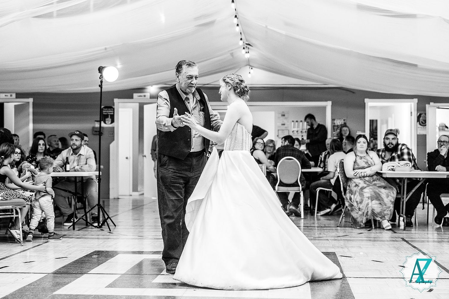 Black and white photo of a bride and groom sharing their first dance at a wedding reception under a tent.