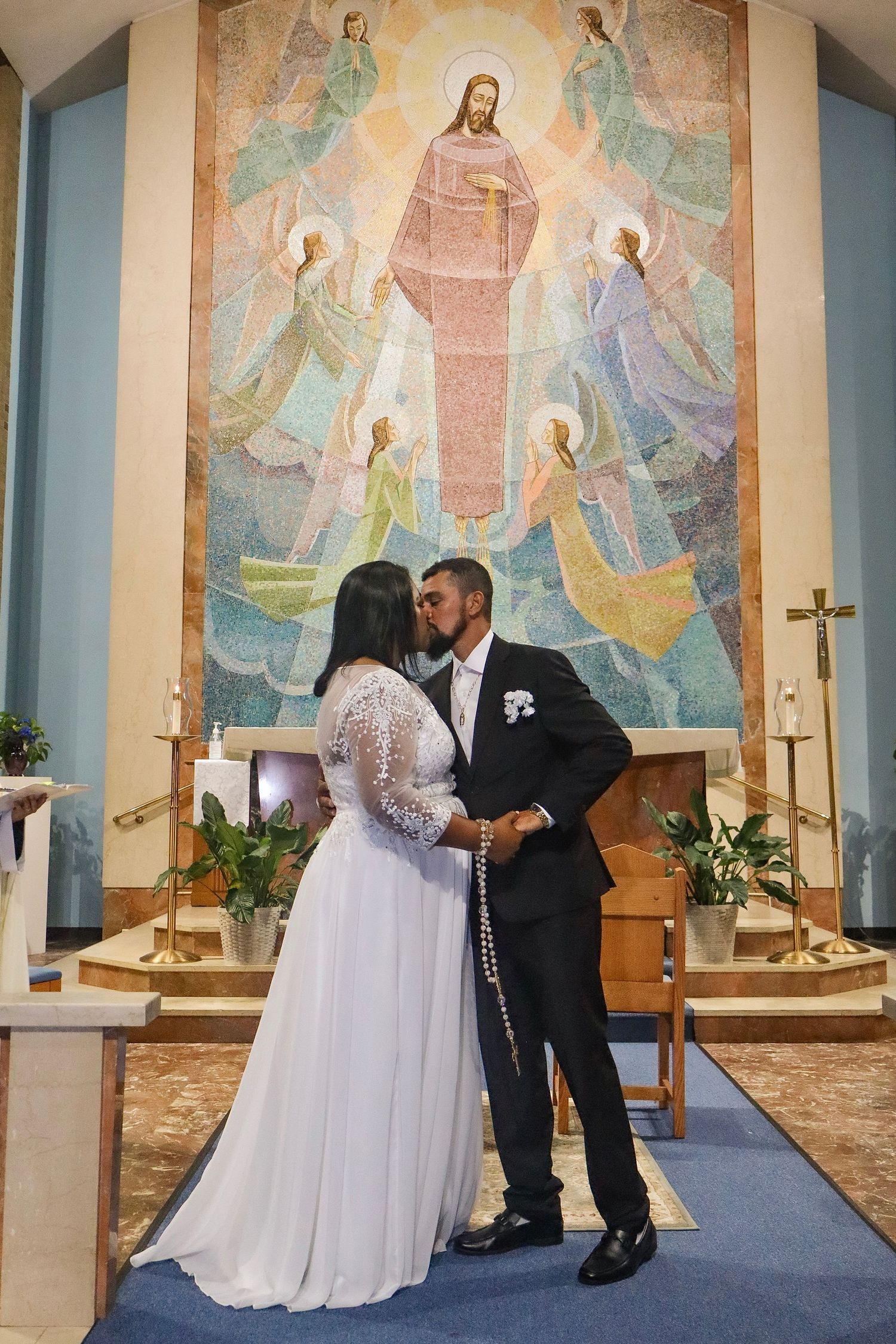 A couple exchanges vows during their wedding ceremony in front of a religious mural.
