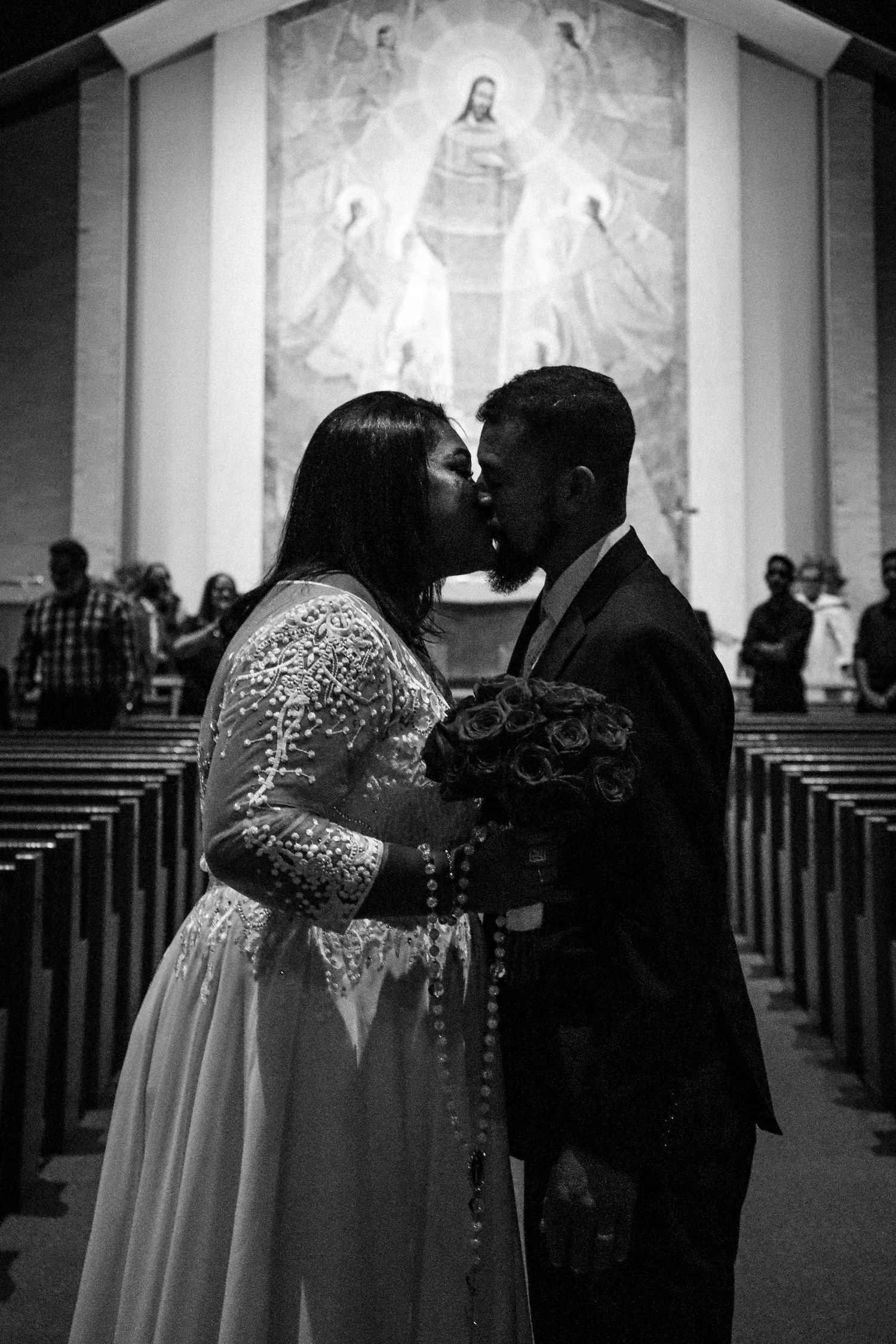 Black and white photo of wedding guests watching a ceremony in a church sanctuary.