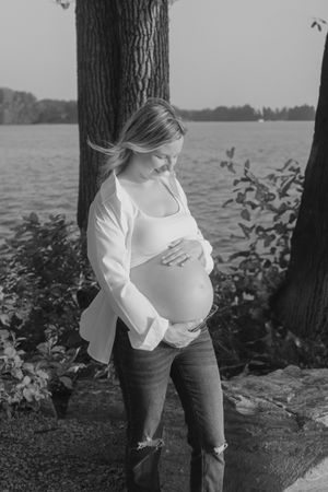 Three black and white photos show a person in a white sweater and dark pants leaning against a tree by a lake.