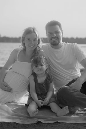A black and white photo series shows a family of three relaxing together on the beach during a casual photo session.