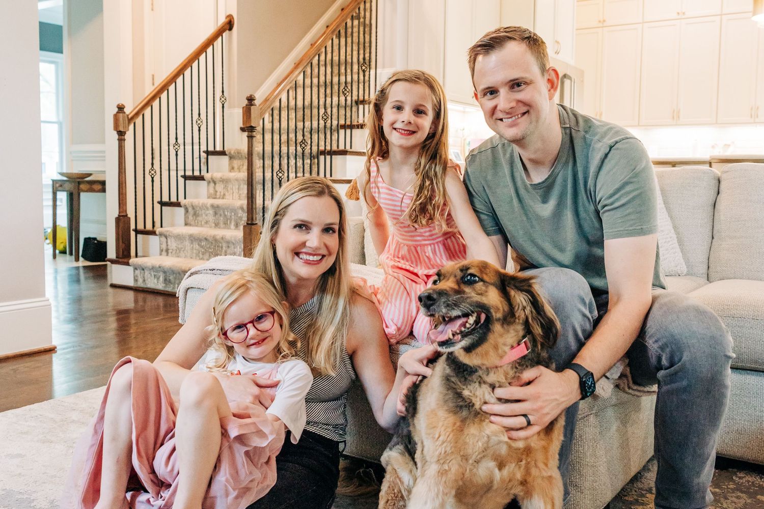 A happy family sits together on their home's stairs with their family dog for Charlotte family photography