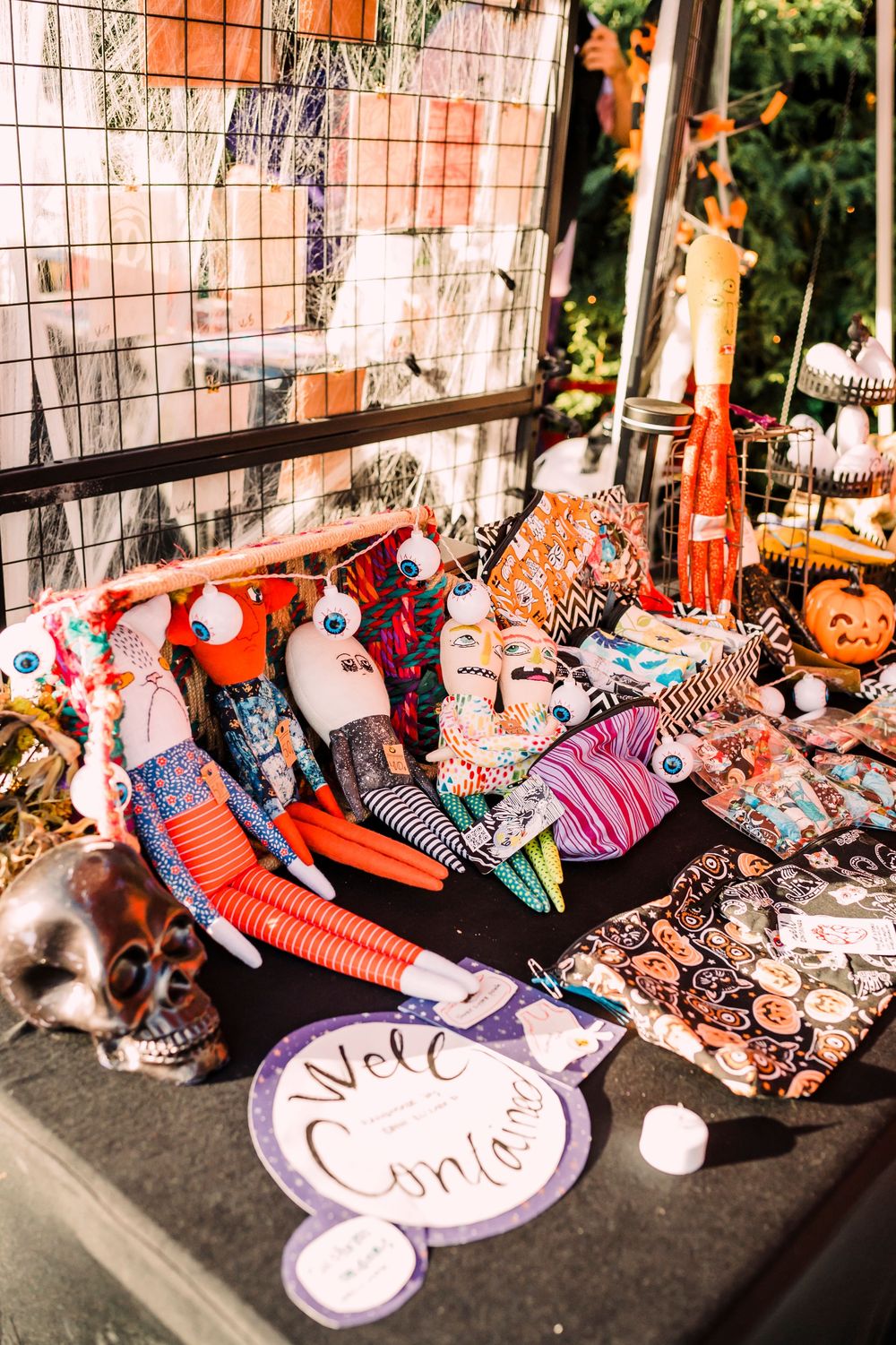 Halloween decor display with orange and black plush toys, skeletons, and spooky festive decorations at a retail booth.