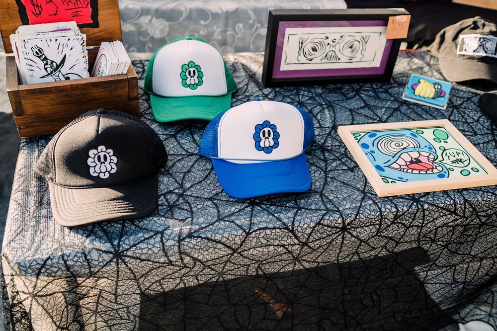 Collection of baseball caps and artwork displayed on a patterned table surface with spiderweb design.