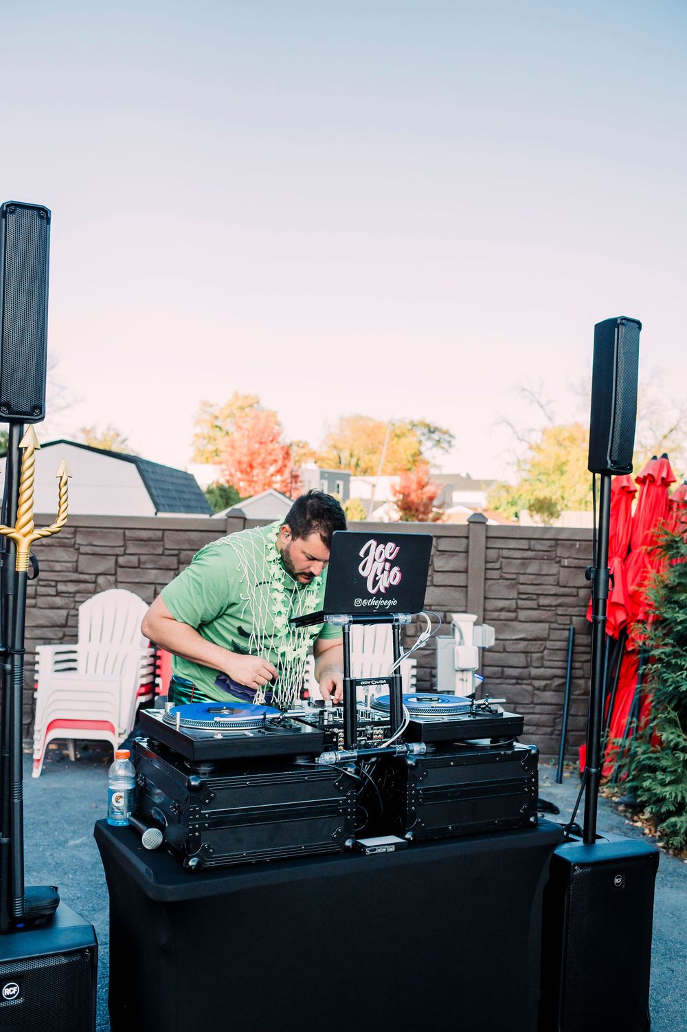 A DJ performs at an outdoor event with professional audio equipment and speakers against a stone wall backdrop.