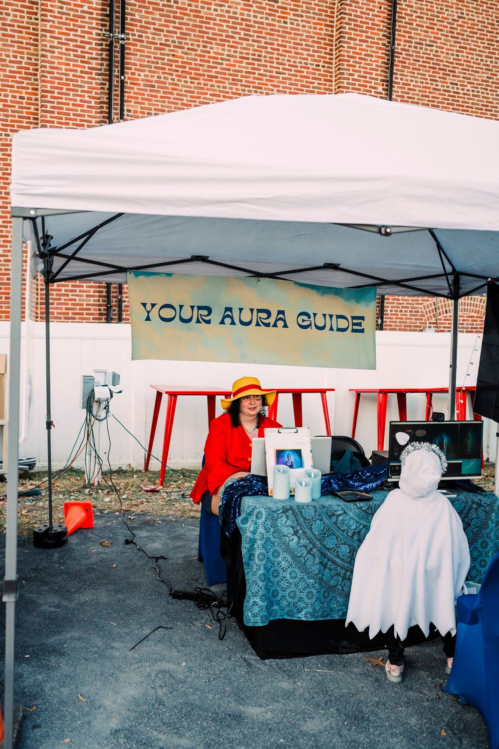 White tent booths set up at an outdoor market with 'Your Aura Guide' sign visible and blue tablecloths.