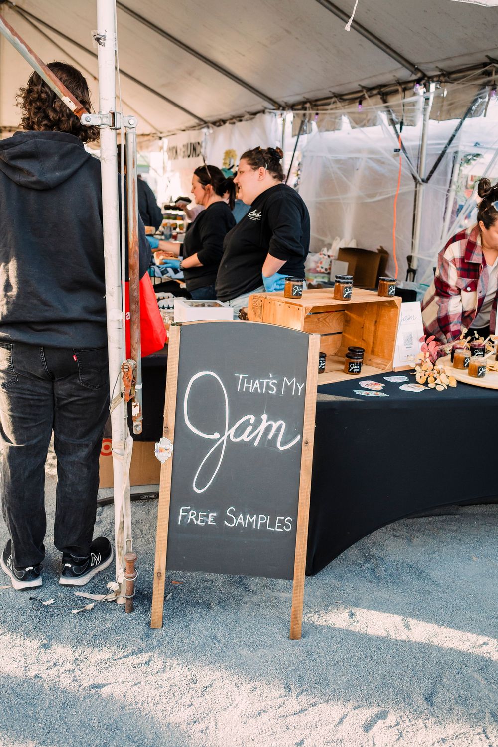 Vendor booth at an outdoor market with chalkboard signs offering free samples.