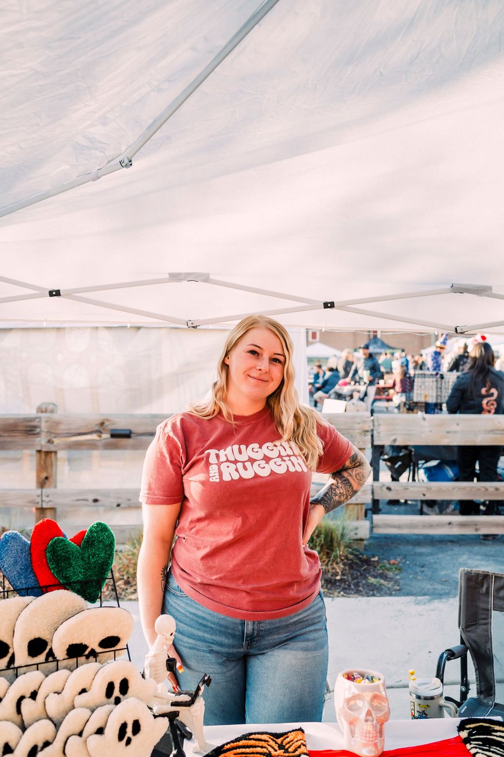 A vendor displays merchandise under a white canopy tent at an outdoor market event.