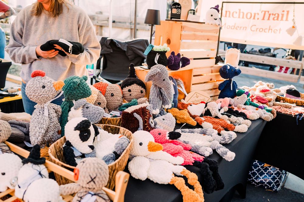 Display table filled with plush stuffed animals and handmade toys at a craft fair.