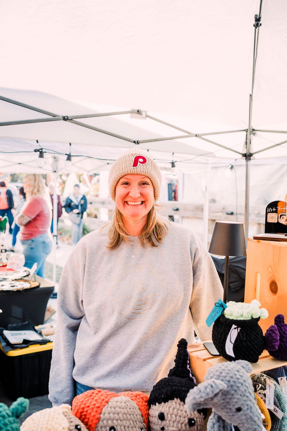 Craft vendor displays handmade items under a white tent at an outdoor market.