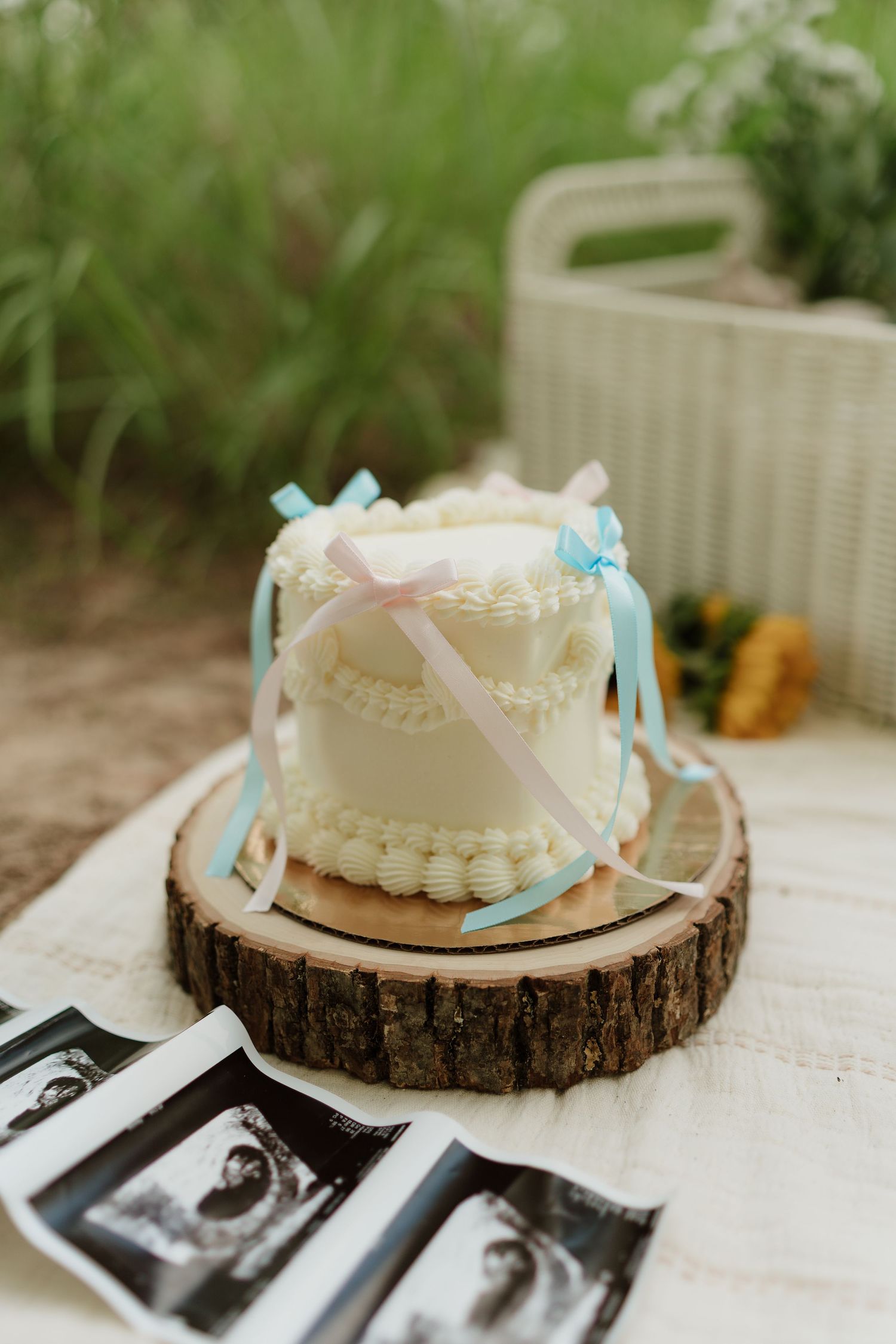 White frosted cake on wood slice with ultrasound photos displayed underneath.