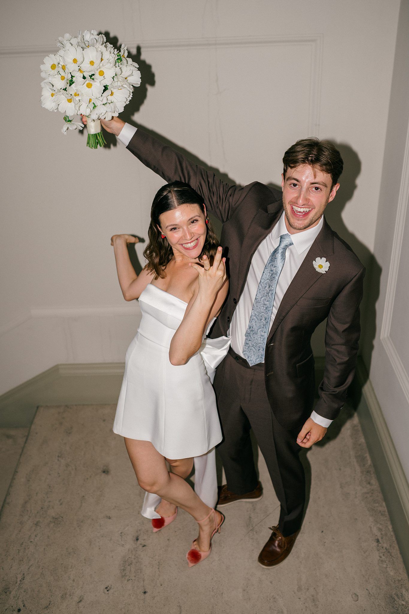 A couple playfully poses and laughs together in a series of four candid wedding photos in a simple hallway setting at elopement in Bath, UK