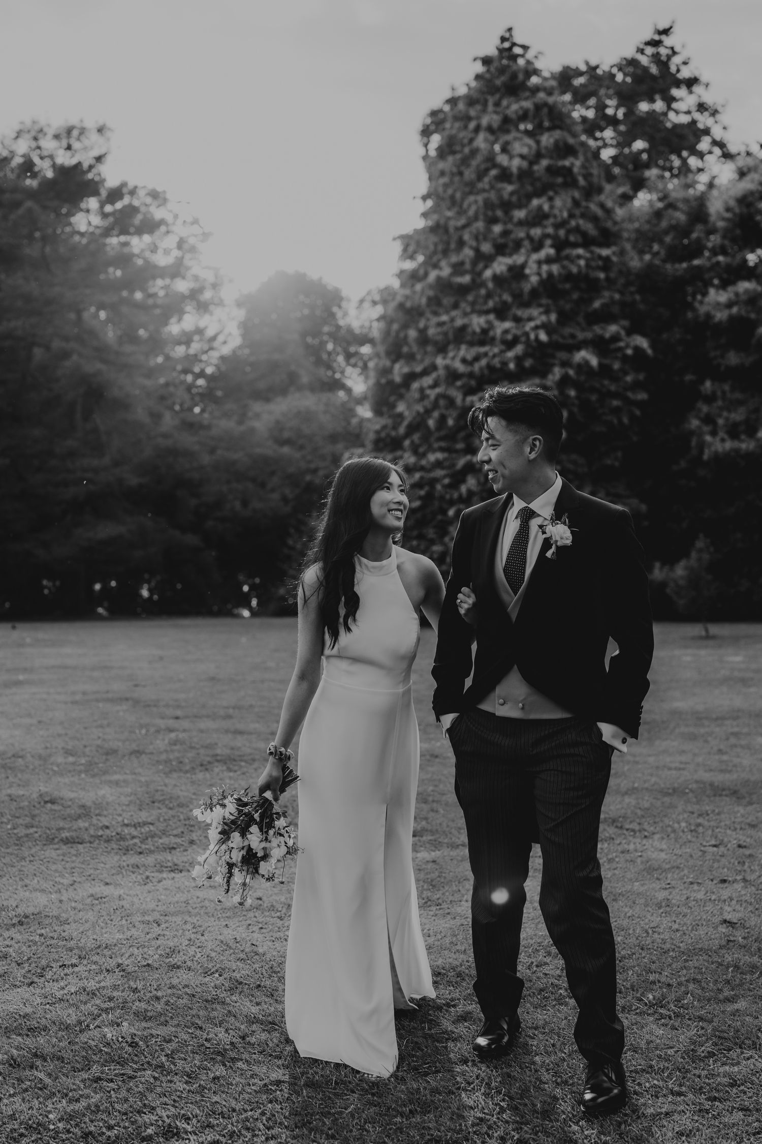 Black and white portrait of wedding couple walking together on garden grounds.