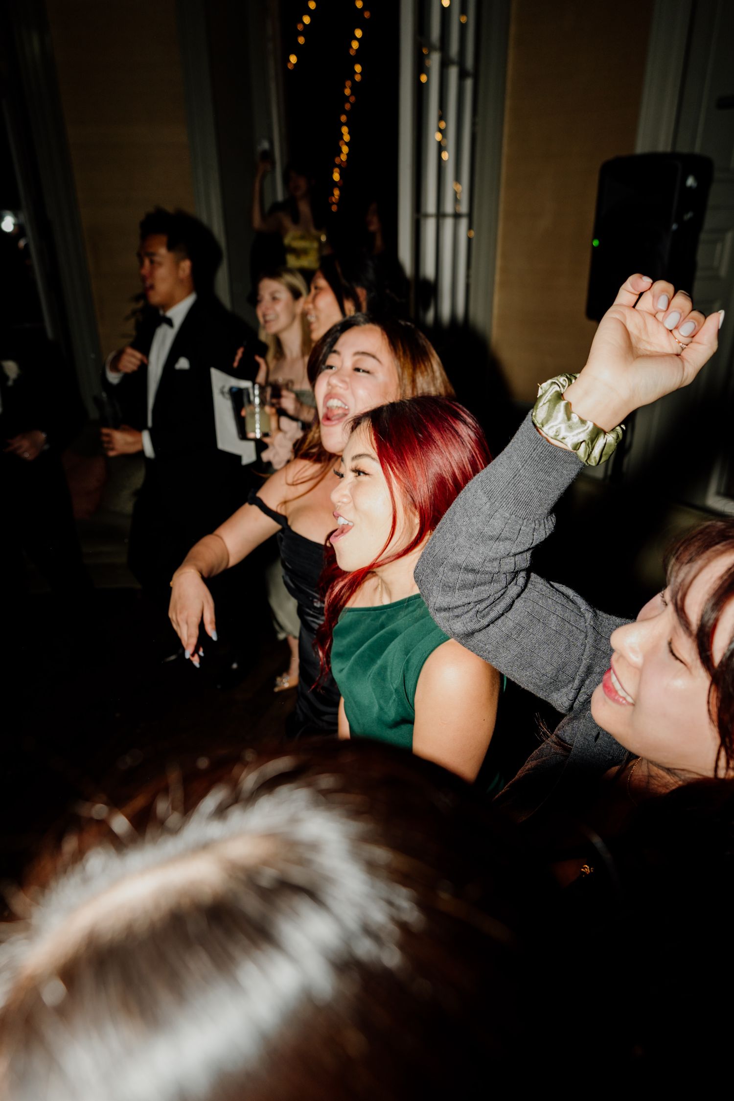 Wedding reception guests dancing and celebrating in a dimly lit venue with string lights.