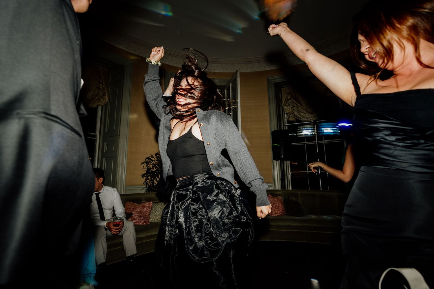 Wedding party dancing in dimly lit reception venue with silhouetted figures.