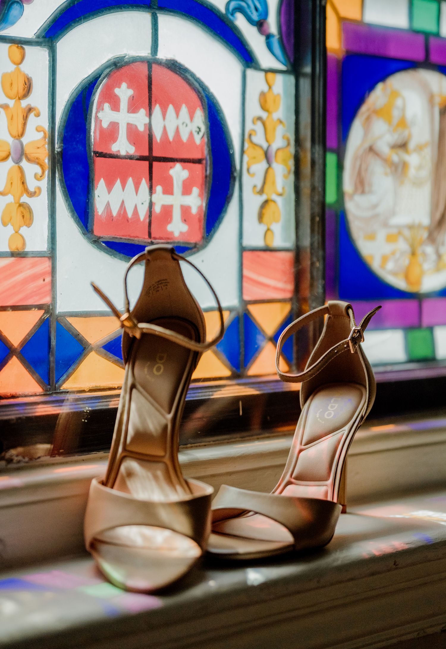 Elegant wedding shoes displayed against colorful stained glass window.