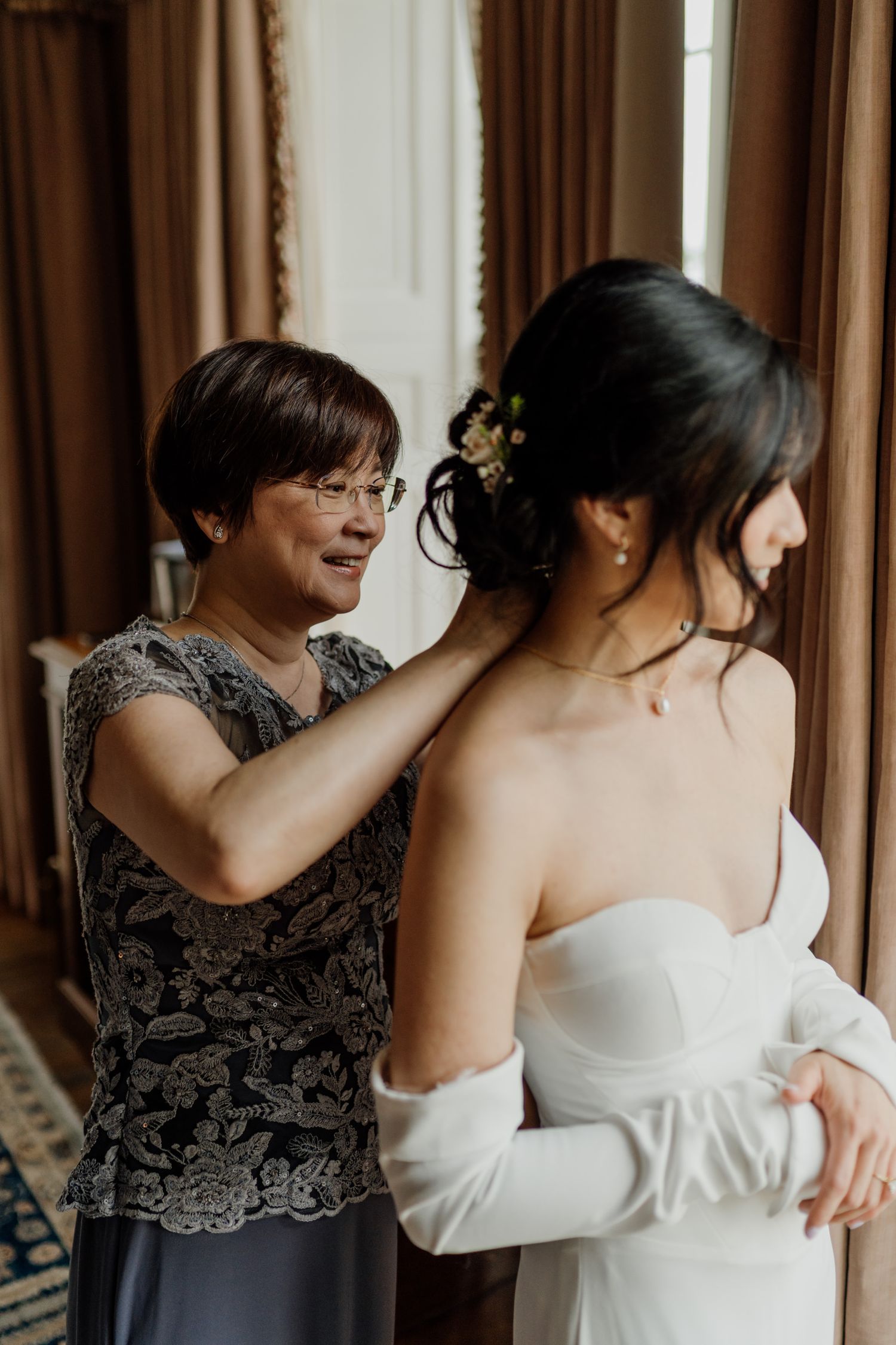 Getting ready moment with a bride in a white wedding dress being helped with final preparations.